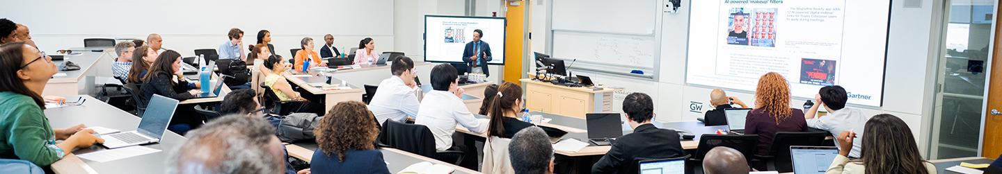 a wide-angle photo of GWSB students in a classroom listening to a lecture