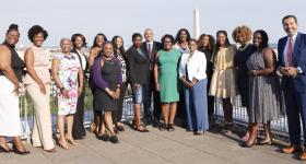 Graduates of the fourth cohort of the ELEVATE program gather for a photo on a sunny day on the rooftop of the Elliott School of Public Affairs building on the GW University campus in downtown Washington, D.C. The Washington Monument is visible in the background. 