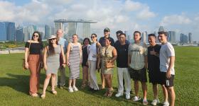 Students in GW's Global Bachelor's Program pose for a photo on a grassy lawn in Singapore. The city skyline with the iconic Marina Bay Sands Hotel is visible in the distance behind them. 