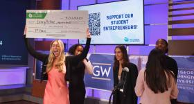 Camryn Baum celebrates her New Venture Competition win onstage, holding up her oversized check for $10,000.